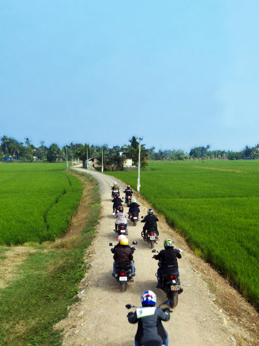 Motorbikes driving down road with green fields either side and blue sky in the background
