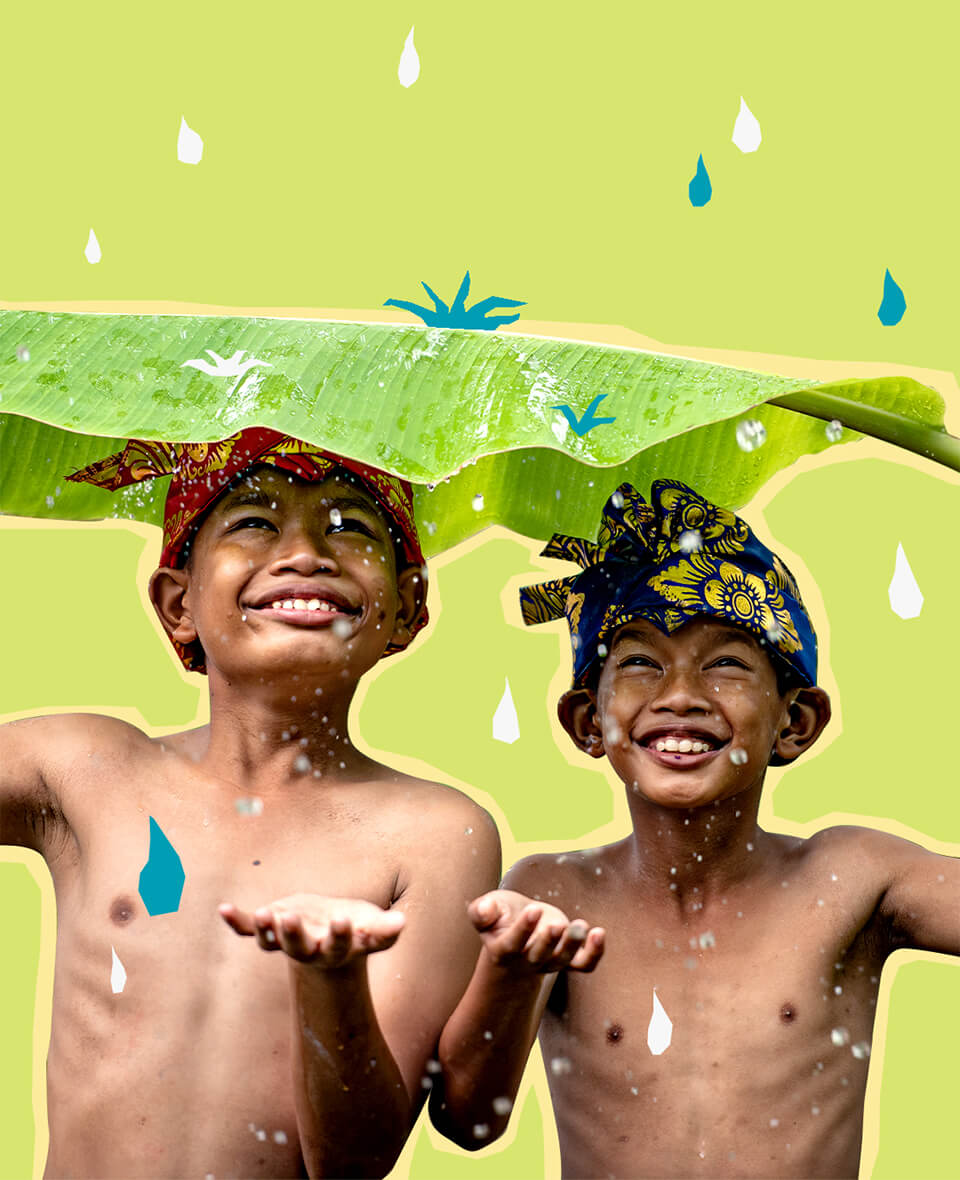 Children smiling whilst standing under large leaf with rain falling